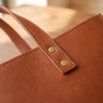 Dettaglio dei manici con rivetti in ottone della borsa tote cognac